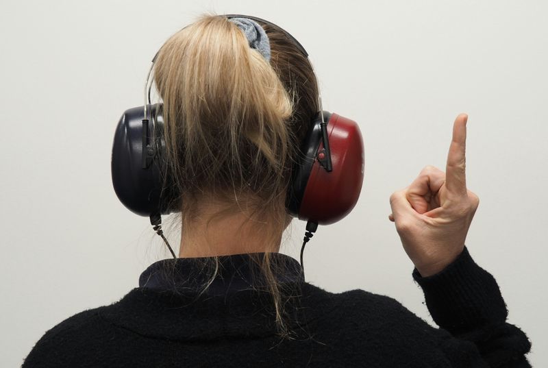 A woman wearing headphones and putting up her finger to show that she's not listening.