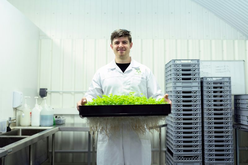 A young man holding a tray of seedlings in a laboratory.