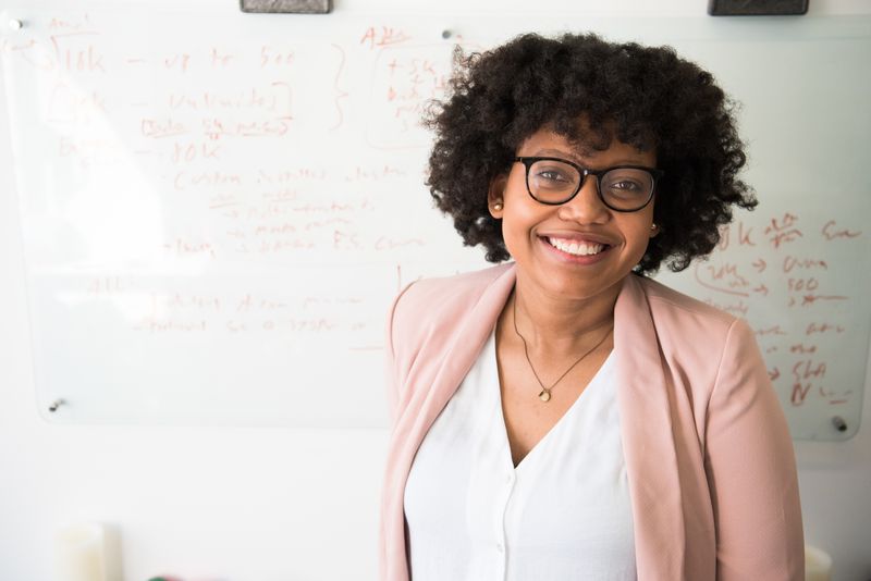 A woman in front of a white board. She is dressed professionally and smiling