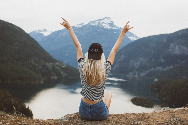 A happy person throwing their hands in the air as they enjoy the view of a mountain lake.