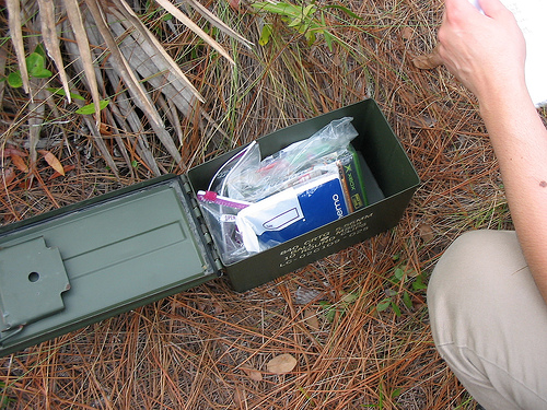 A green geocache container opened in the woods.