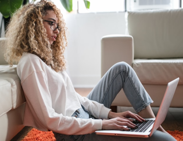 A girl sitting on the rug typing on the computer. 