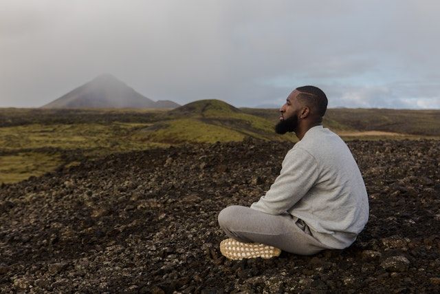 Man sitting cross-legged on the ground, looking out across an empty field.