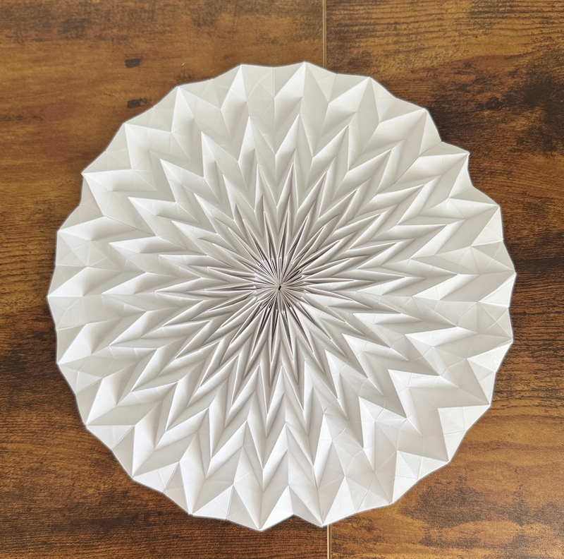 A white origami tessellation with repeating folds on a wooden surface..