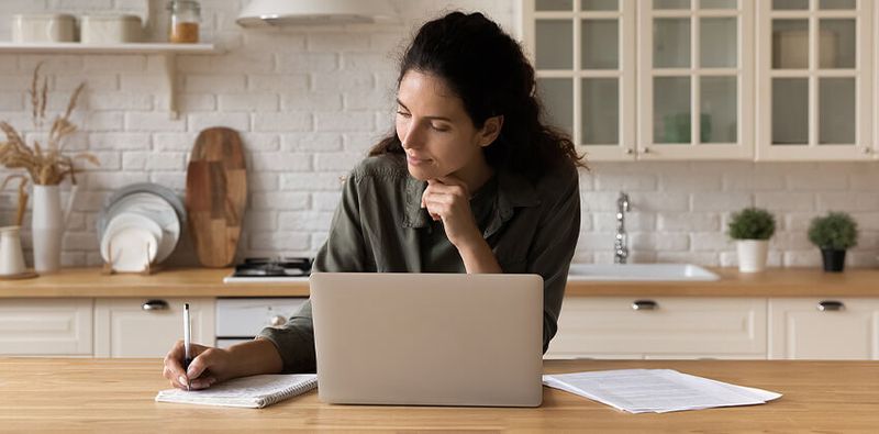 A woman sitting in front of her laptop and writing down something on paper.