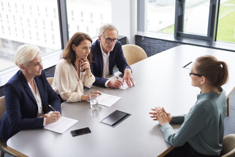 A woman at a job interview. Three senior managers ask her questions in a conference room.