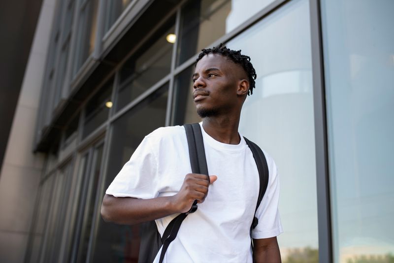 A confident black youth carrying a backpack and walking on a city street.