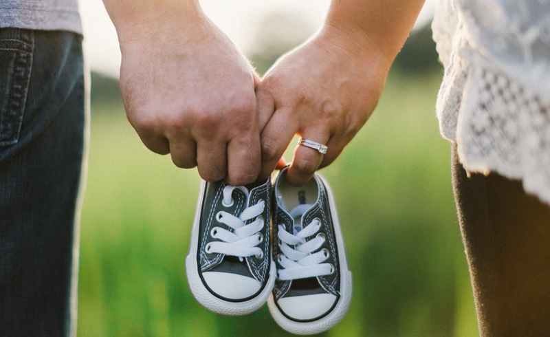 A man and woman walking outside holding hands with toddler shoes in between their fingers.