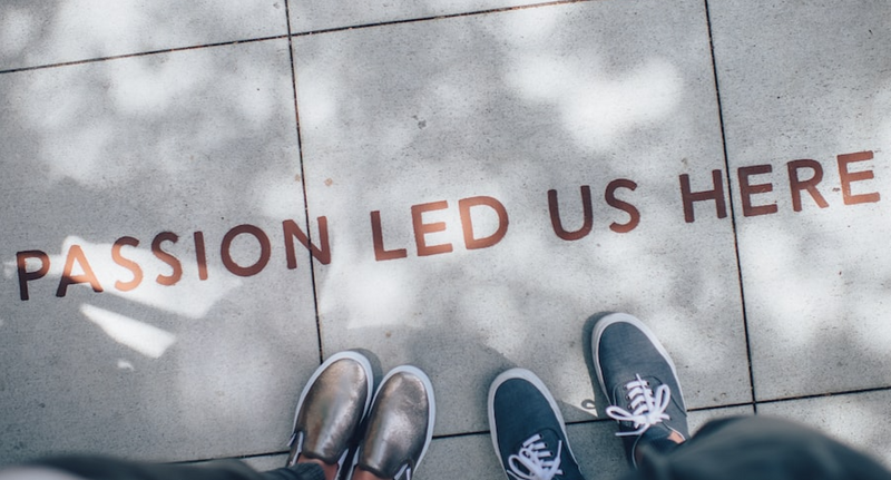 over head view of text on a sidewalk that reads passion led us here with two pairs of feet standing next to it