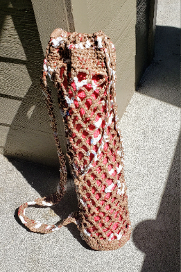 A water bottle holder with a carrying strap, made with plarn.