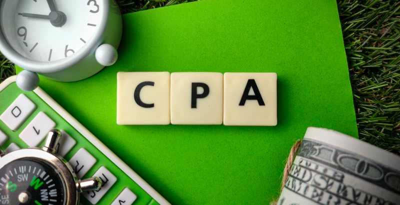 Top view of a clock, calculator, compass, money, and blocks with the letters CPA on a green background