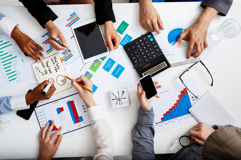 Business people's hands on white table with documents, a calculator, and devices.