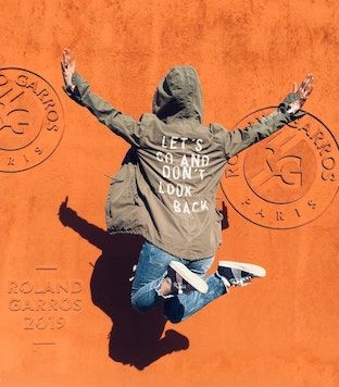 Person jumping against a orange wall. Back of the jacket reads let's go and don't look back.