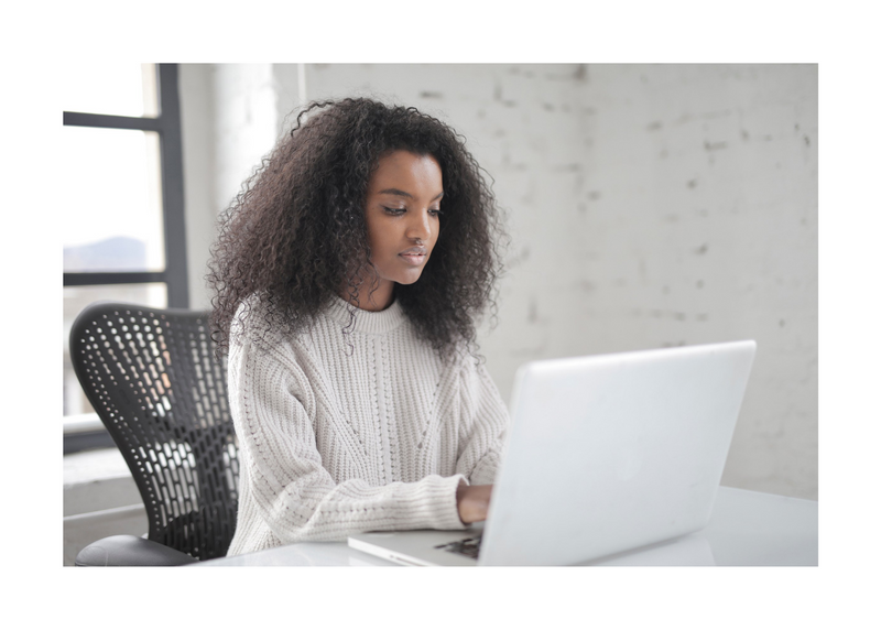 Woman sitting at a desk in a well-lit room typing on laptop 