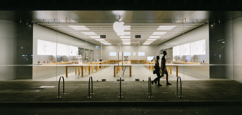 Two people walking in front of an Apple Store.
