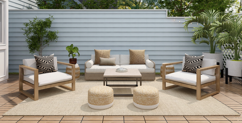 An outdoor patio with a large rug underneath a set of chairs, a couch, footstools, and a table.