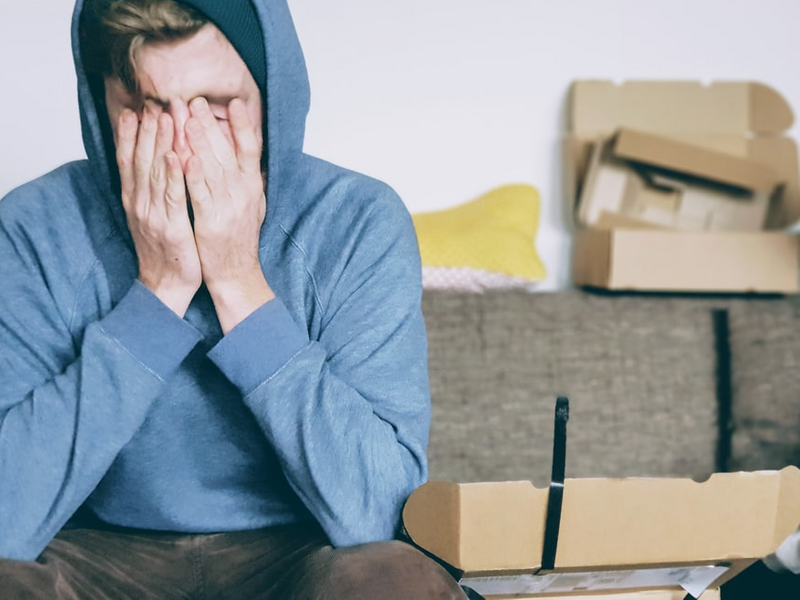 Man sitting on couch with hands on his face and open boxes around him.