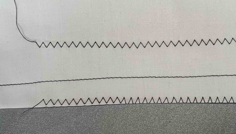 Photograph of lines of zigzag and straight stitching on a piece of folded fabric.