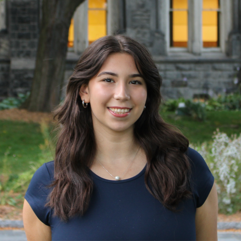 Lucy poses for a photo in front of a campus building at her university.