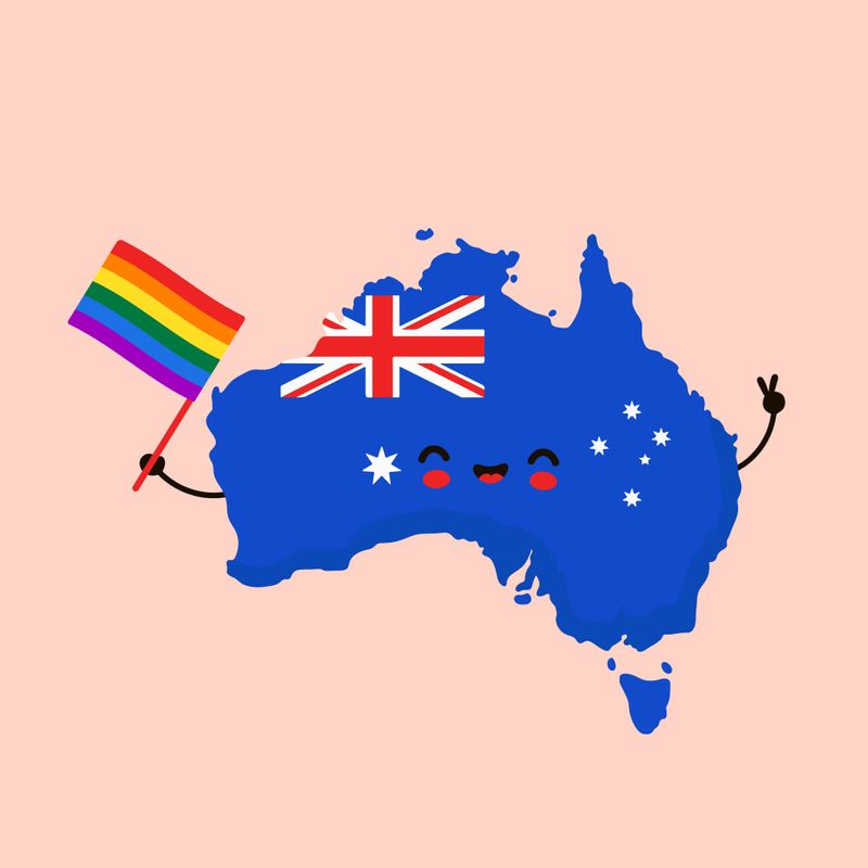 A map of Australia as a cartoon charatcer. It holds a rainbow flag in one hand and shows the peace sign with the other hand.