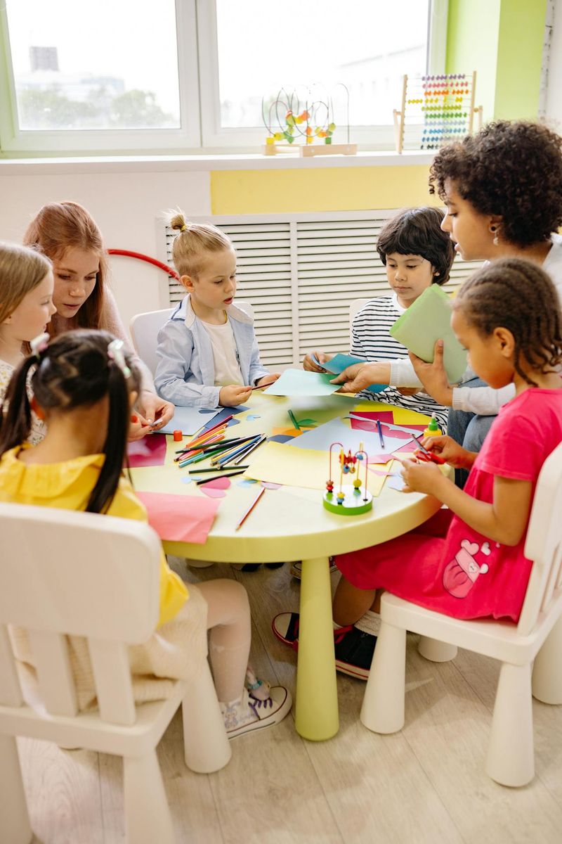 A teacher at a table answers questions from students who are working on origami.