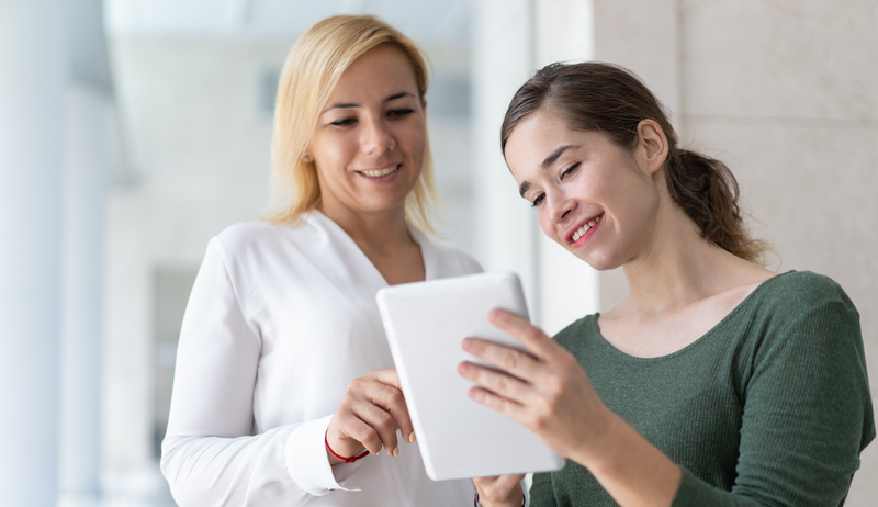 Two women smiling while looking at a tablet.