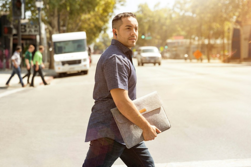 A man wearing earbud walking across street looking around holding folder