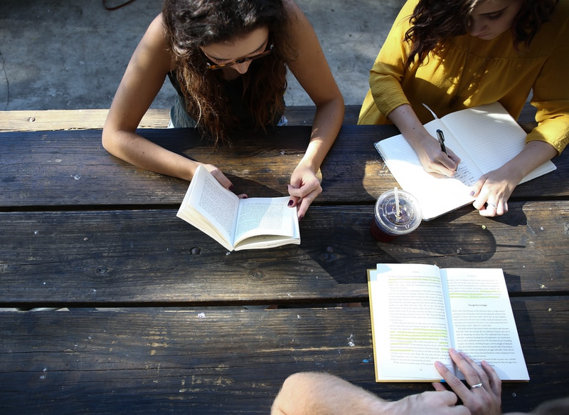 Three people reading outside at a picnic table