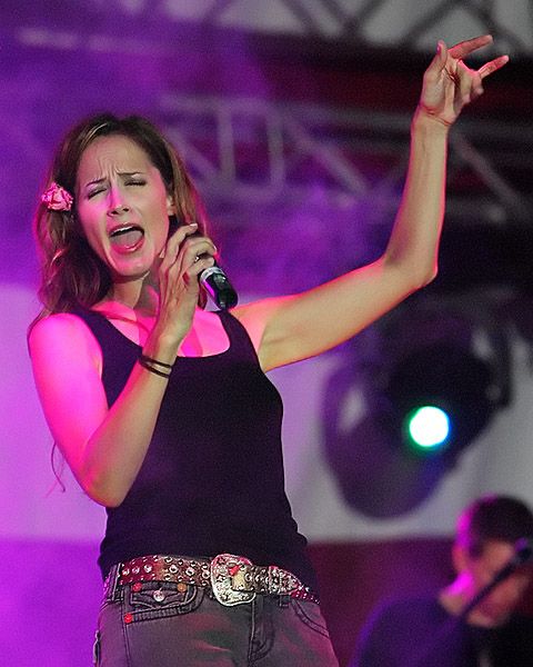 Chely Wright on stage singing into a microphone, hand raised, wearing a western belt buckle