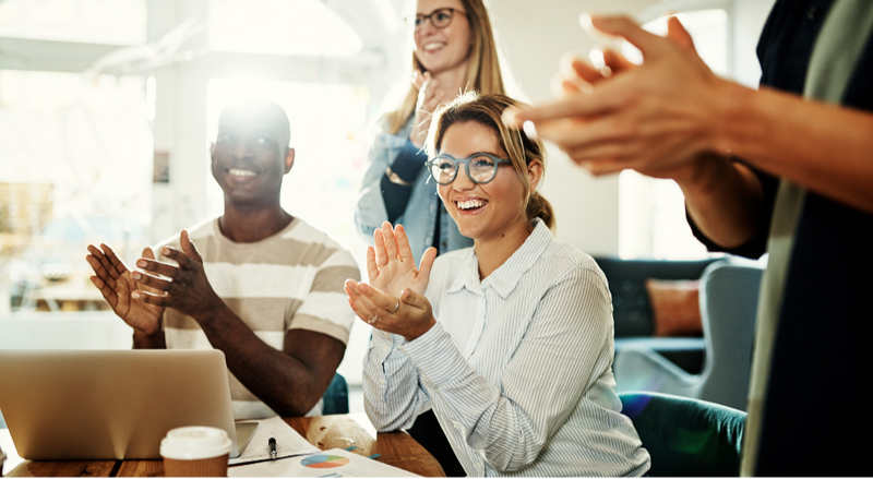 A happy group of people at work from diverse backgrounds clapping their hands