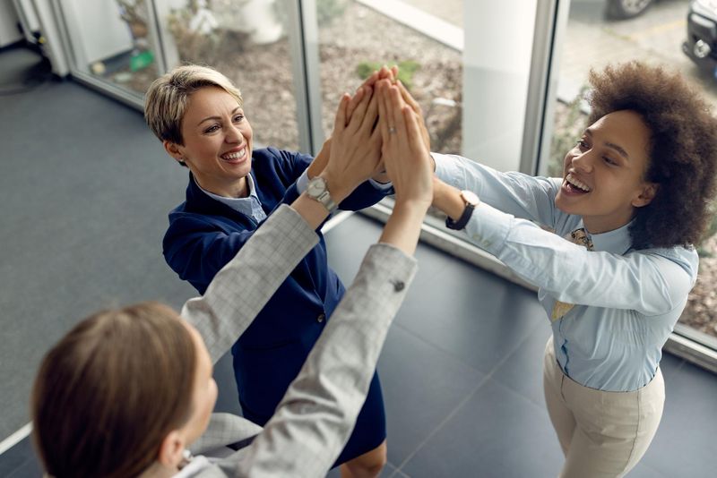 Three coworkers high-five in an office, celebrating teamwork and a shared achievement.