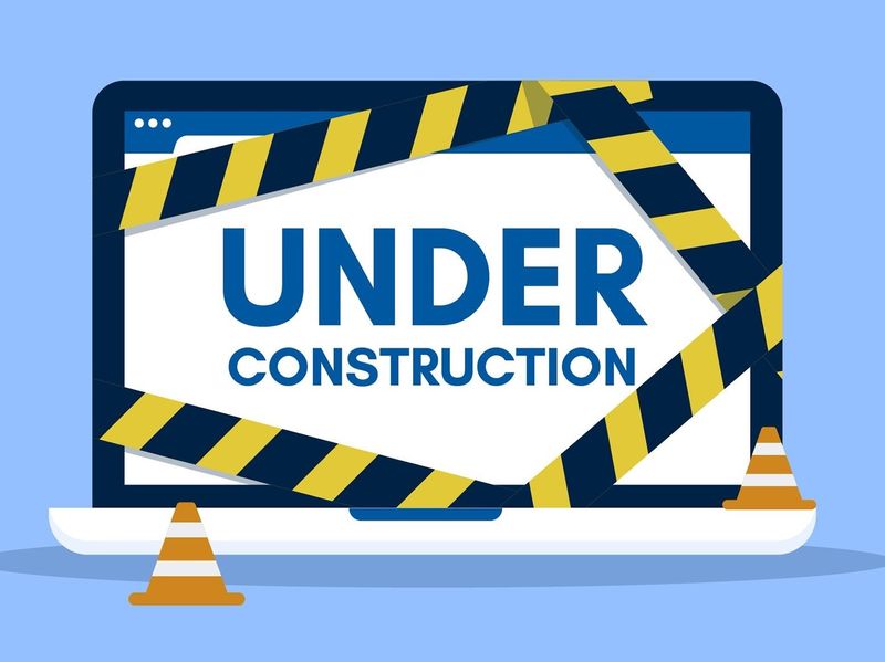 A laptop behind yellow and black tape and orange cones with the words 'under construction' on the screen.