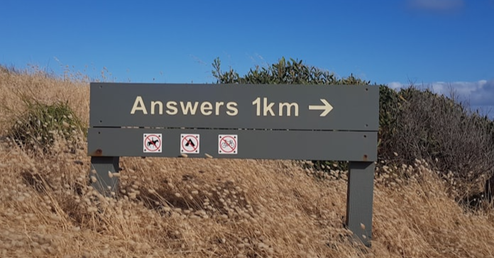 A trail sign in a field with "Answers: 1km written" on it.