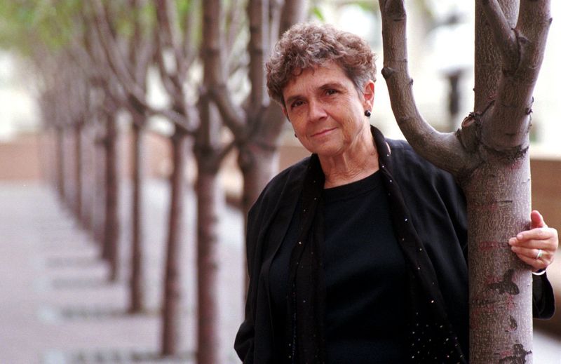 Adrienne Rich posing while leaning on a tree in an urban park.