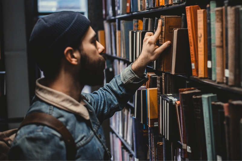 A person leafing through books on a university library shelf.