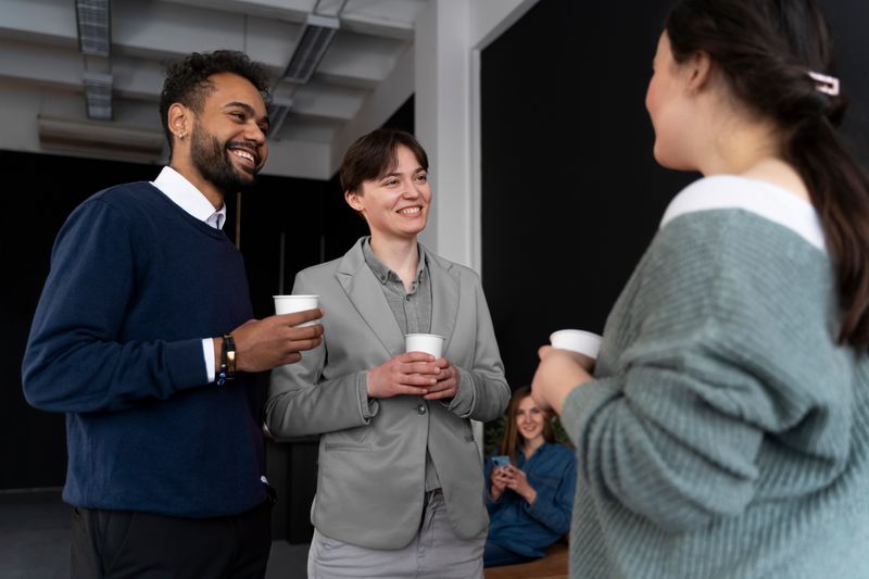 A group of three professionals standing holding coffee cups, engaged in conversation.