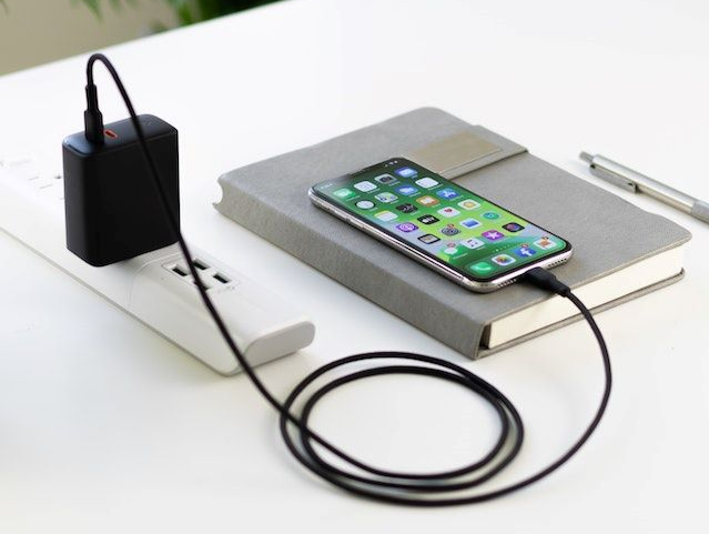 Recharging smartphone from power strip on top of a diary laying on a white office desk