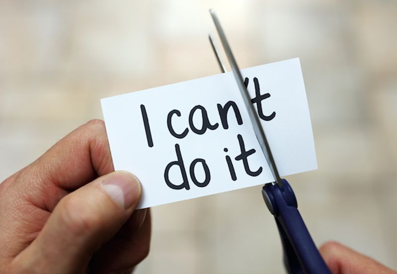 A person using scissors to cut the 't' off of the word can't on a small piece of paper.