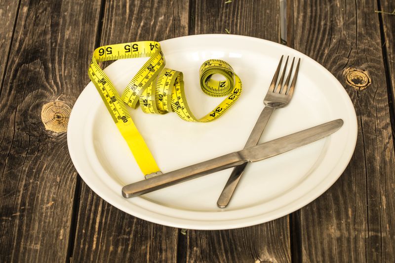 White plate with a yellow tape measure and silver cutlery on it but no food.