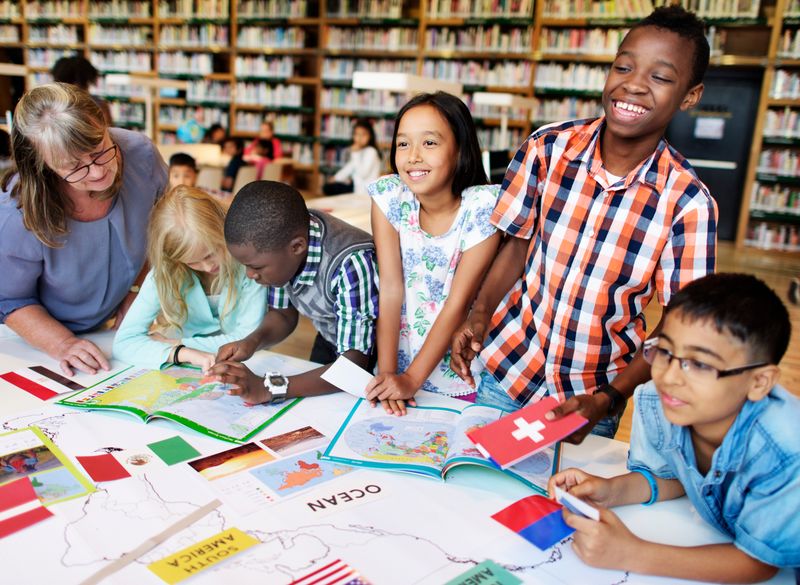 Students work together on a project while a teacher peers over one student's shoulder. 