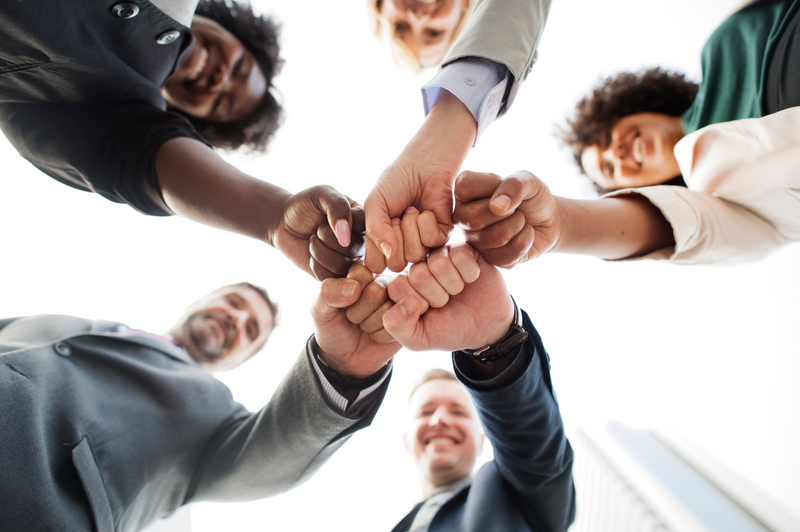 A diverse team of workers standing in a circle putting their fists together, signifying teamwork.