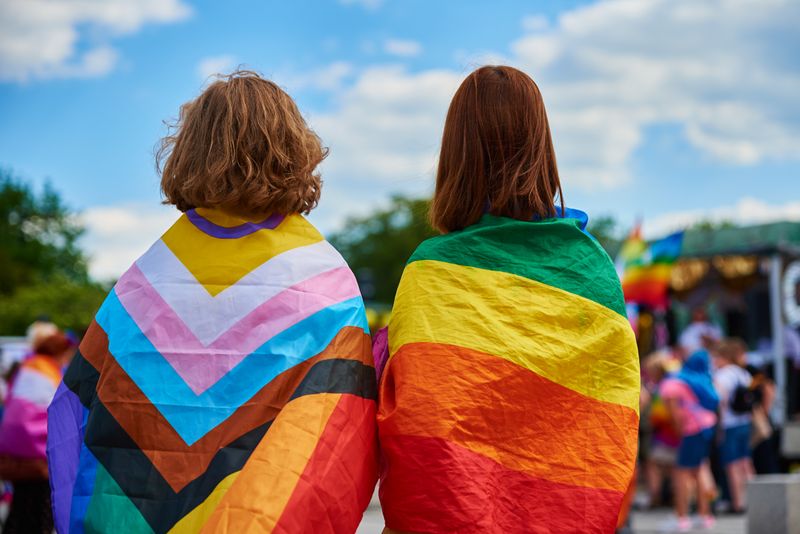 Image of two people with pride flags wrapped around their shoulders