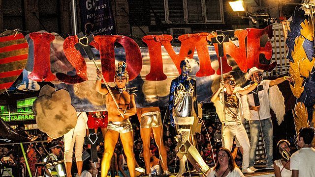 A float at the Sydney Gay and Lesbian Mardi Gras. A group of people wear shiny angel costumes and dance under a sign.