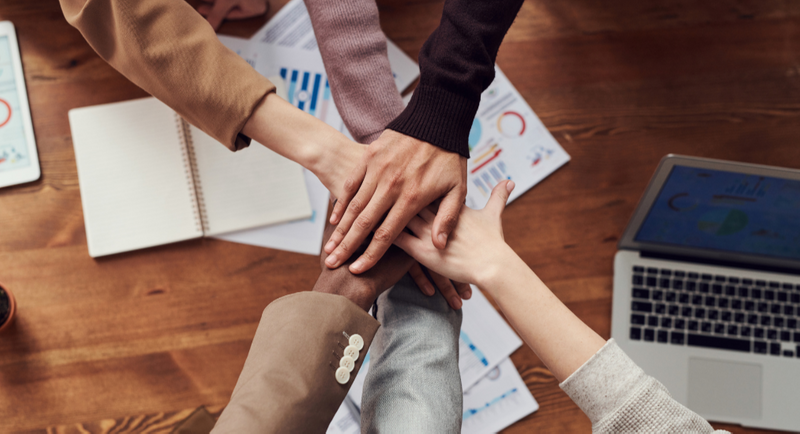 A group of people at work placing their hands on top of each other. 