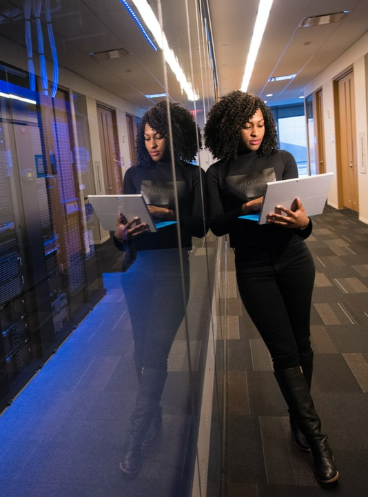 data engineer holding a laptop while standing beside a glass wall in a server room