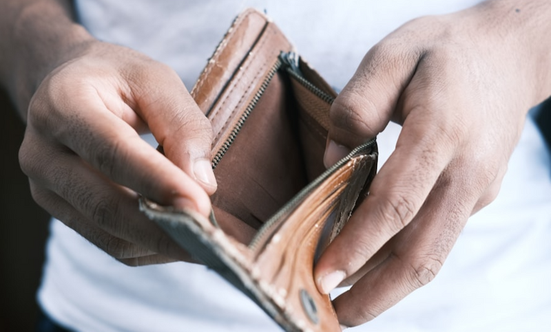 A person looks at his empty wallet, symbolizing financial struggle or disappointment.