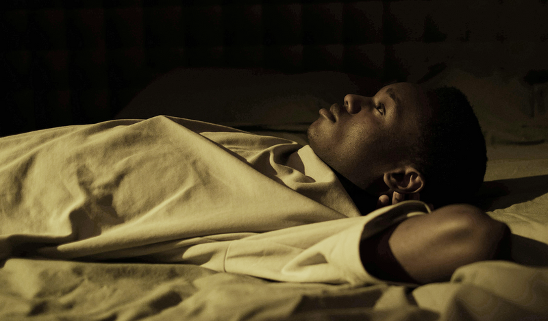 A man lying in bed at night, staring at the ceiling, appearing deep in thought