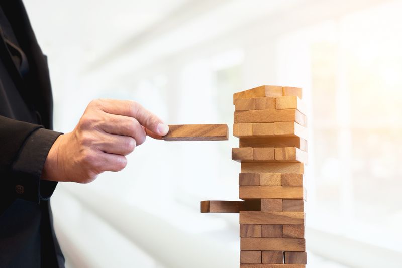 A hand removes a wooden block from a stacked tower, illustrating risk identification and decision-making.