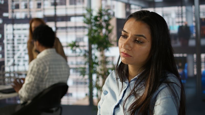 A woman in an office looking sad while her coworkers don't notice.