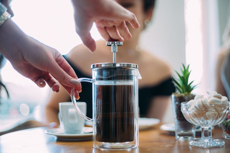 A person pressing down a pot of coffee with a french press 